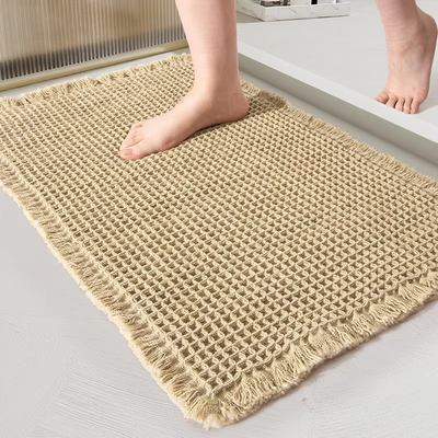 Beige waffle bath mat by Mattona with fringed edges, bare feet stepping onto it