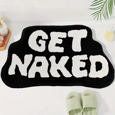 Black GET NAKED bath mat by Mattona with white lettering, flat front view with slippers below